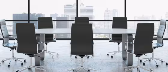 Modern conference room with a long table, eight black chairs, and large windows overlooking a city skyline.
