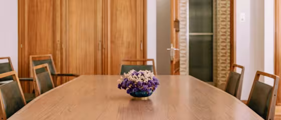 Wooden conference table with brown chairs and a vase of purple and white flow