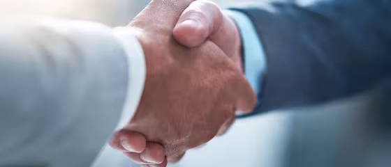 Two people in business attire shaking hands, symbolizing agreement or partnership, with a blurred background.