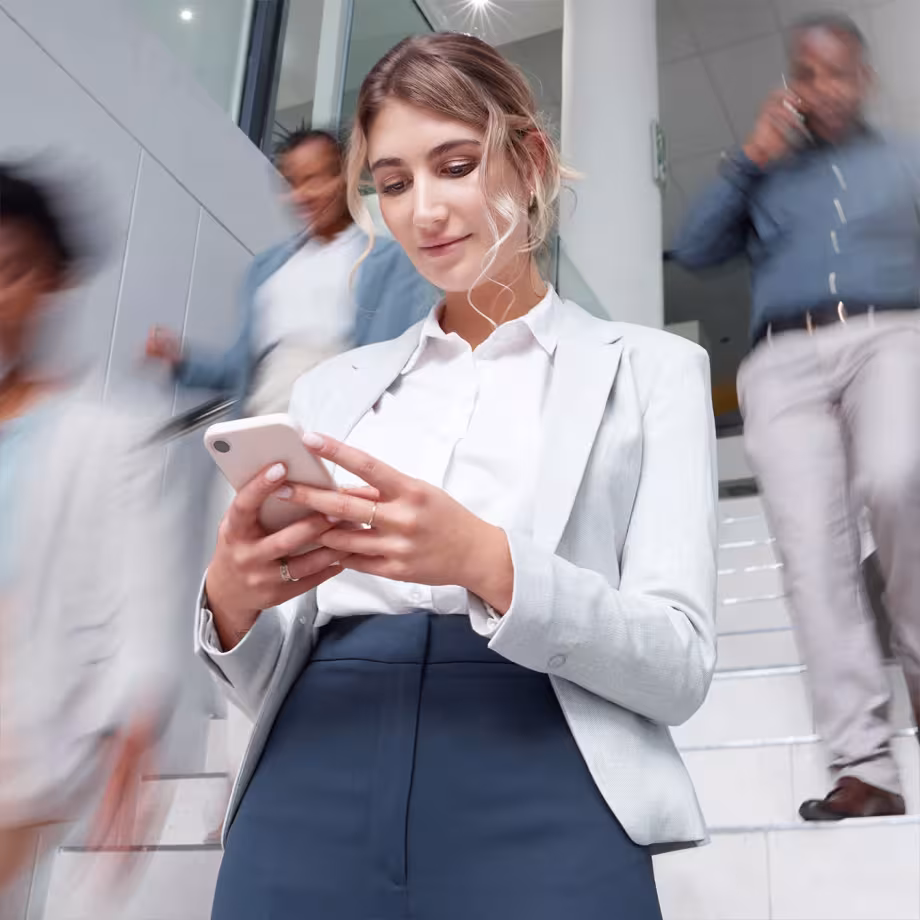 Businesswoman in a gray suit checking her phone while walking down steps.