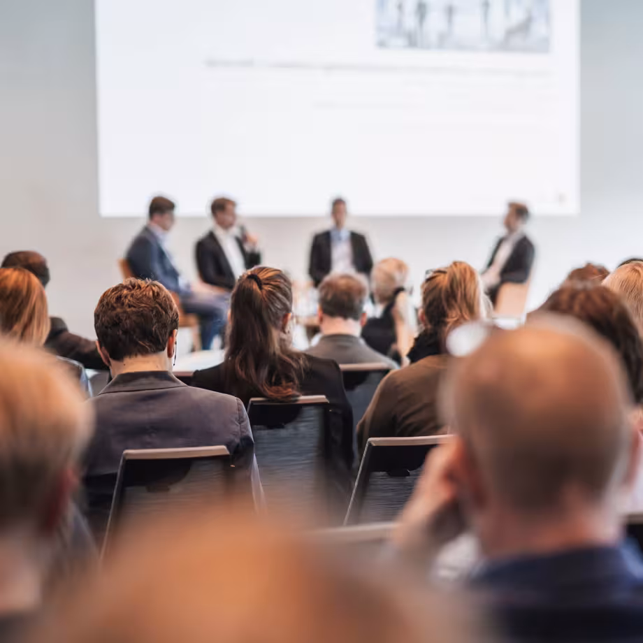 Audience seated facing a panel of four speakers at a conference.