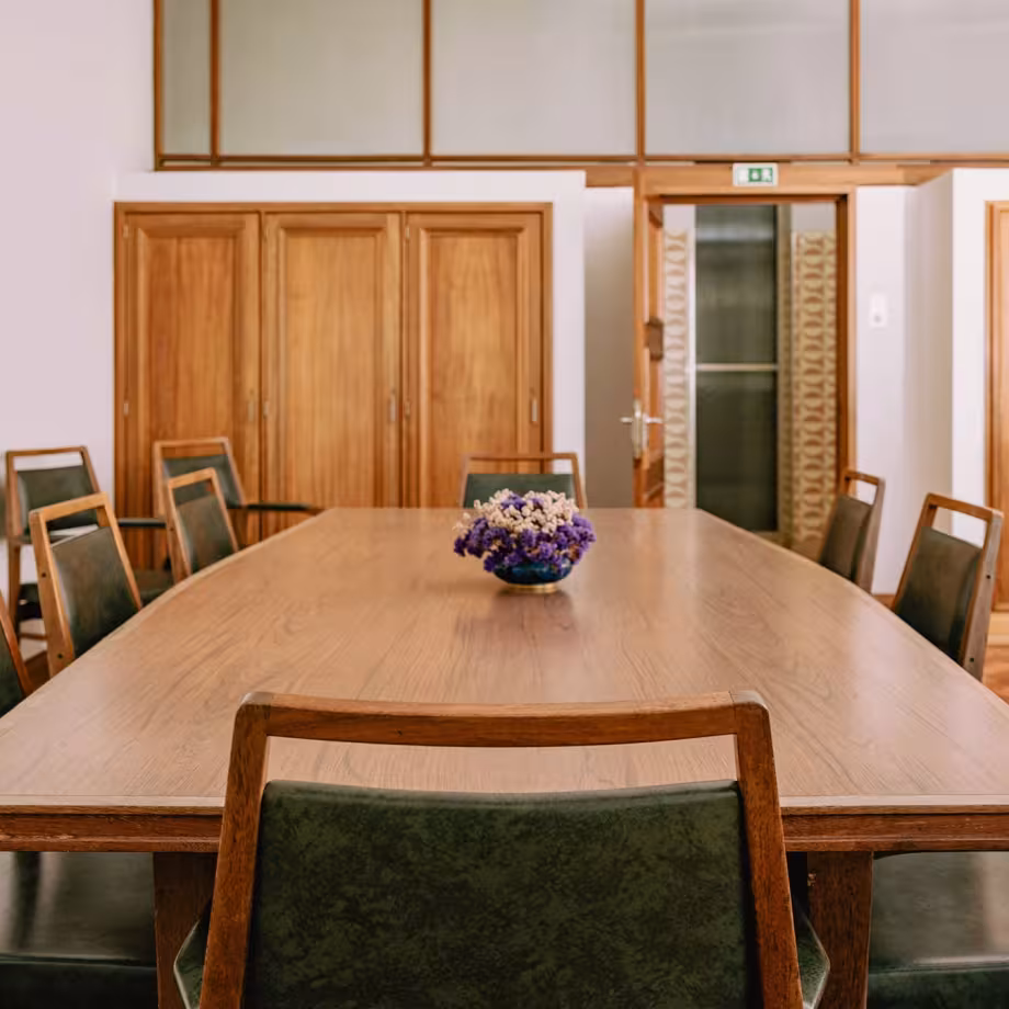 Wooden conference table with brown chairs and a vase of purple and white flow