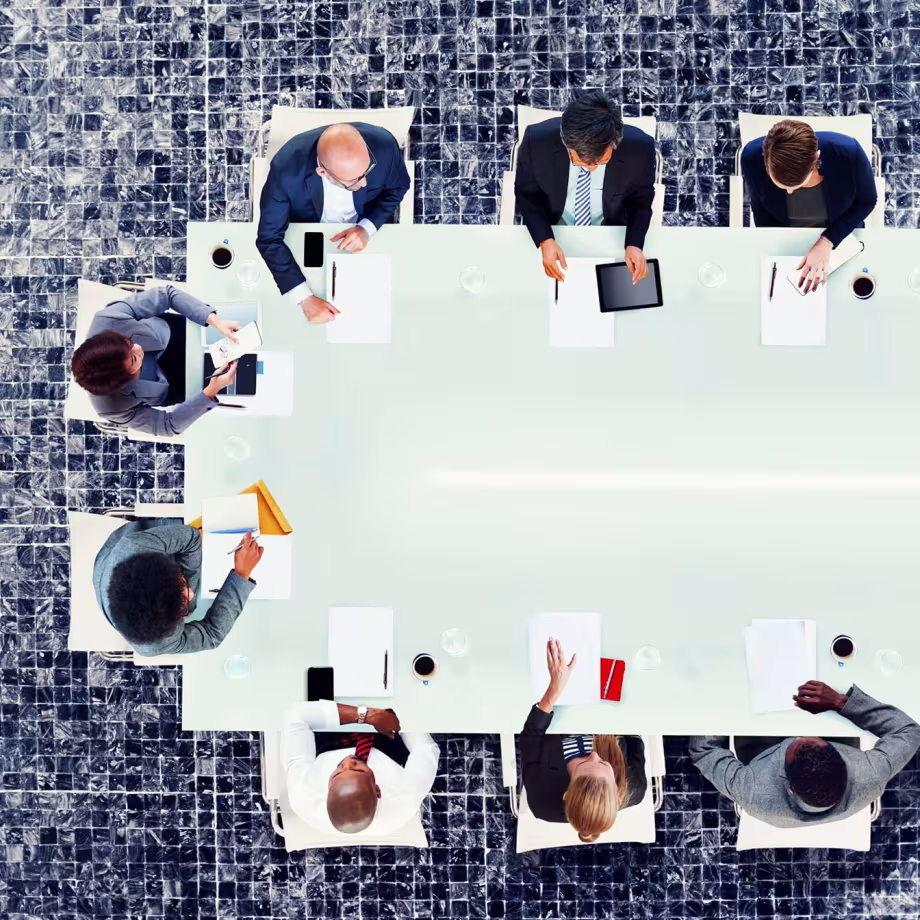 People seated around a glass conference table in a business meeting.