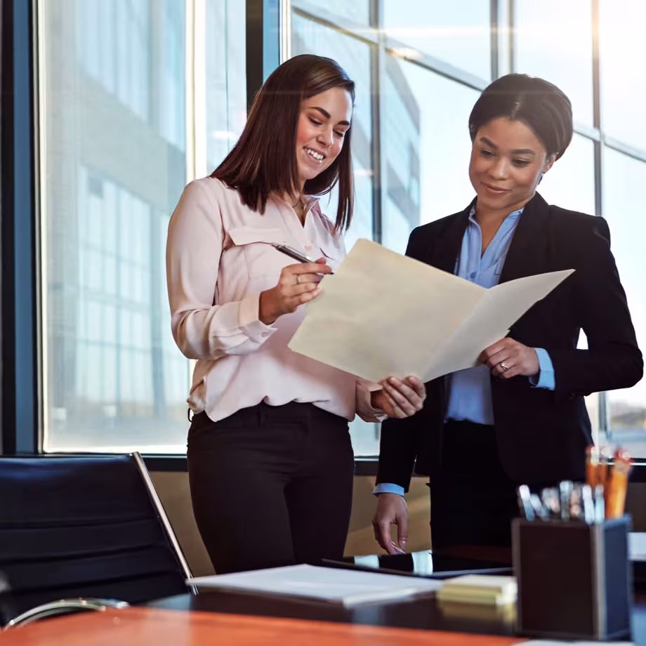 Two women in business attire reviewing a document in a modern office.
