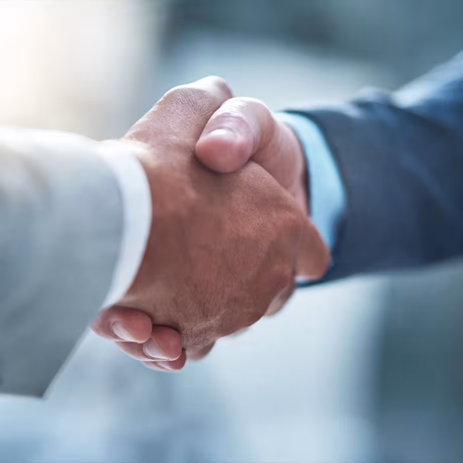 Two people in business attire shaking hands, symbolizing agreement or partnership, with a blurred background.