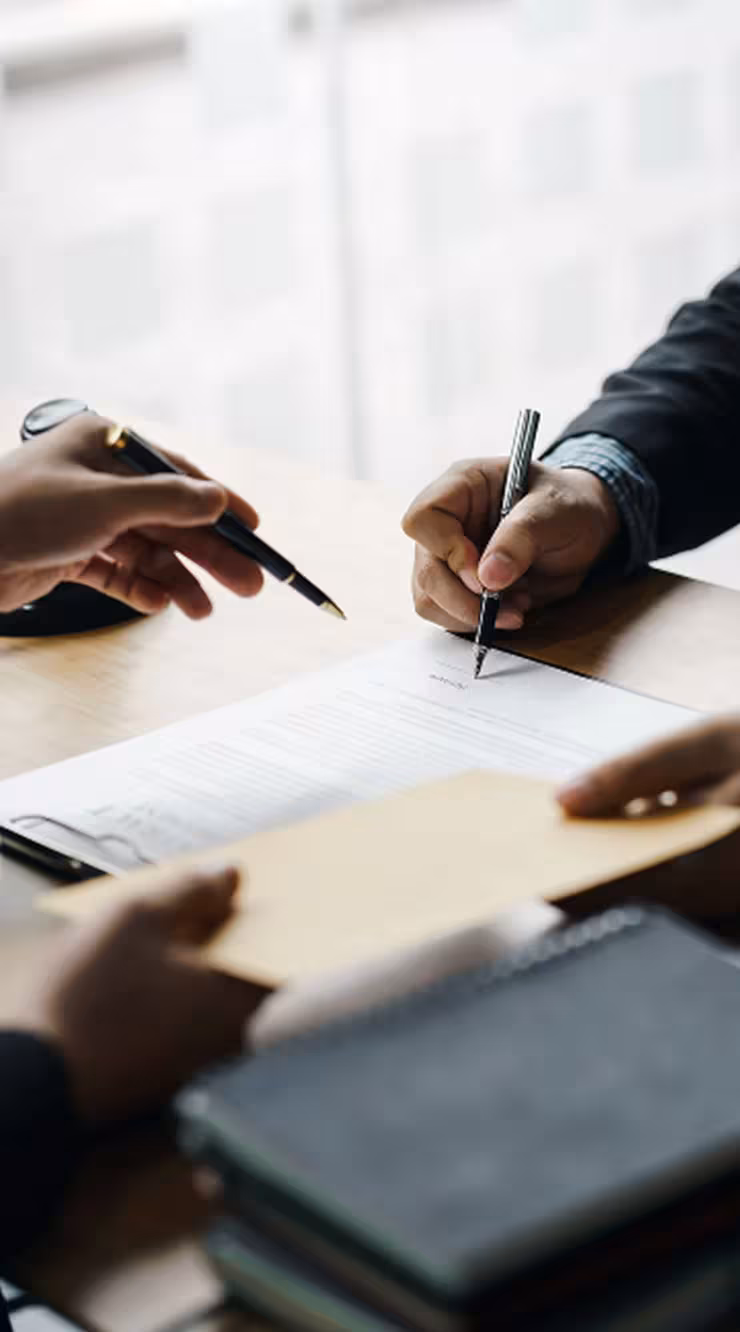 Three people seated at a table reviewing a document with pens.
